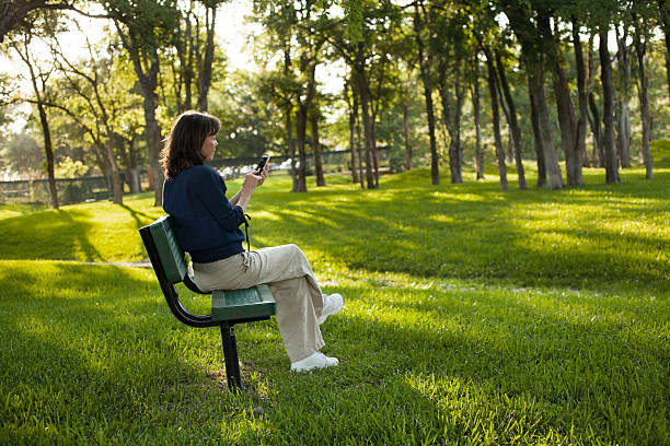 istock Mature woman sitting on park bench.  Texting in summer. 540974938