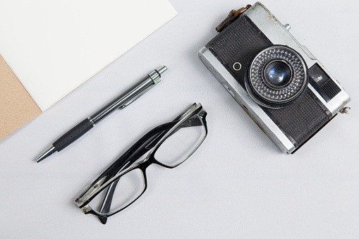 notebook with pen , glasses and camera on desk with white fabric background