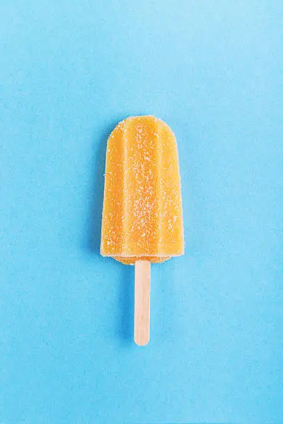 Single homemade orange popsicle on a blue background. Top view with copyspace