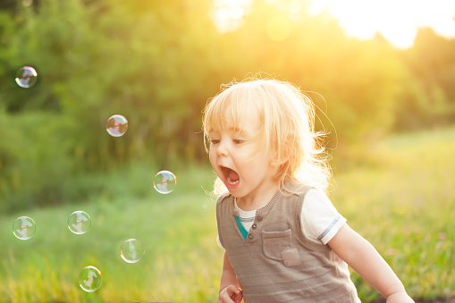 Little blonde boy playing with soap bubbles in a park.