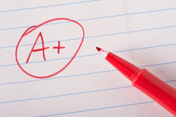 A plus (A+) grade written in red pen on notebook paper with the pen sitting there.