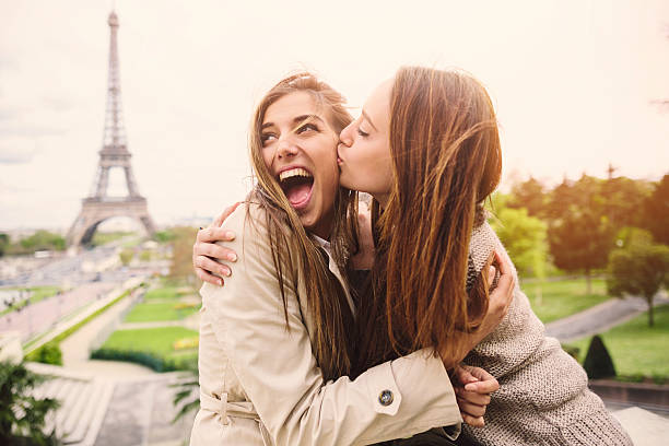 Friends in Paris Girl kissing her friend in front of the Eiffel Tower in Paris. gay long hair stock pictures, royalty-free photos & images