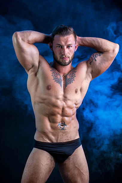 мышечный молодой человек, стоящий без рубашки - swimming trunks men muscular build athlete стоковые фото и изображения
