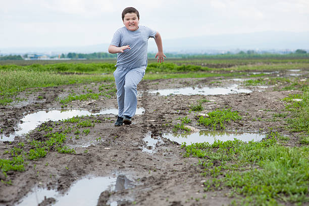 fat boy running in   field among the mud and puddles