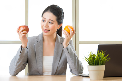 Young asian businesswoman eating healthy snack, orange and apple