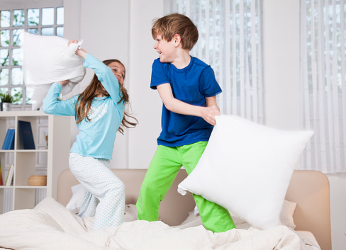 Two children fitting with pillows on a bed in a bedroom. Very active pillow fight.