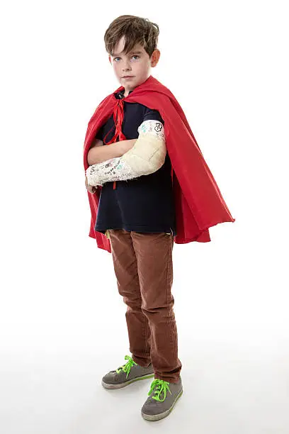 Studio shot of a young boy dreaming of becoming a superhero although he has a broken arm