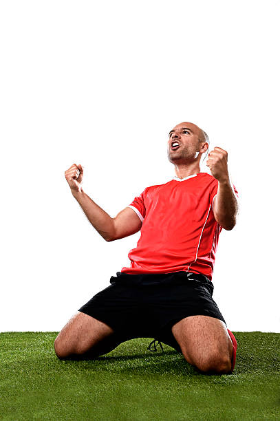 happy excited football player celebrating scoring goal kneeling on pitch stock photo