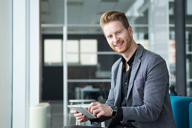 istock Smiling businessman sitting in office hallway holding digital tablet. 541130540