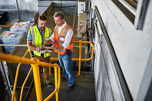 Tracing and tracking in the warehouse Shot of two warehouse workers standing on stairs discussing papework caution step stock pictures, royalty-free photos & images