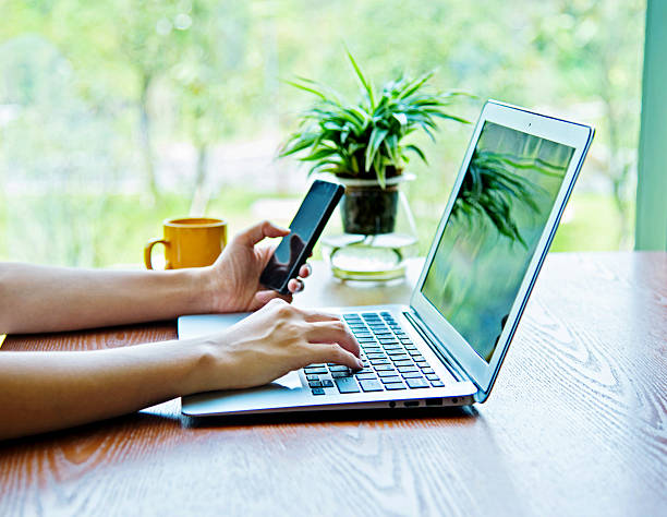 Woman using phone and laptop in a coffee shop.