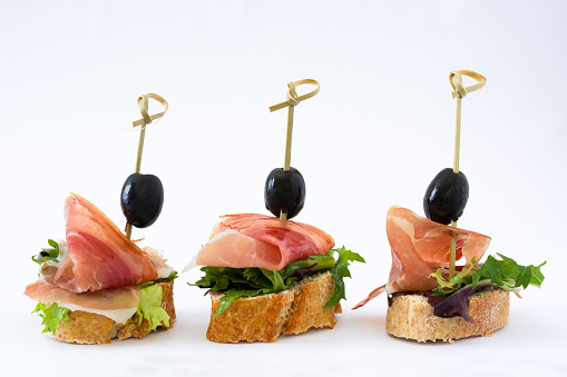 Spanish serrano ham skewer with olive and lettuce isolated on white background