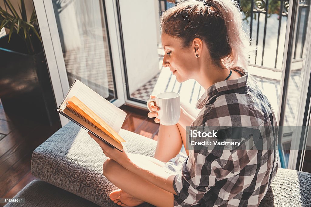 Young pretty woman Young pretty woman  sitting at opened window drinking coffee and reading a book enjoys of rest Balcony Stock Photo