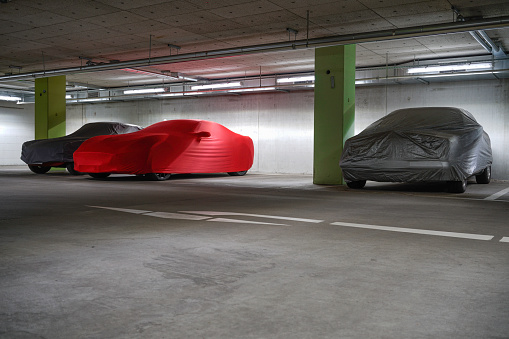 luxurious cars under protective covers in a parking garage