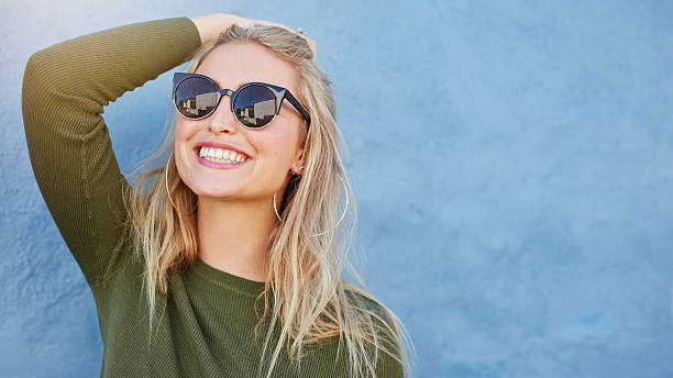 Stylish young woman in sunglasses smiling Close up shot of stylish young woman in sunglasses smiling against blue background. Beautiful female model with copy space. beauty fashion model adult beautiful stock pictures, royalty-free photos & images