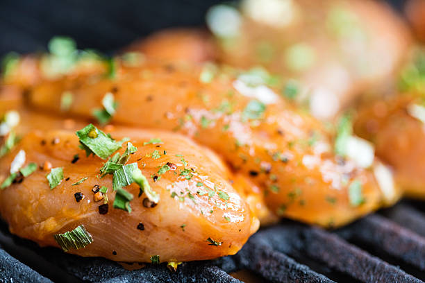 Raw marinated chicken breasts cooking on the BBQ grill.