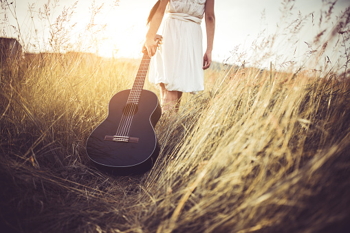 cropped view of a woman pulls a guitar through a field