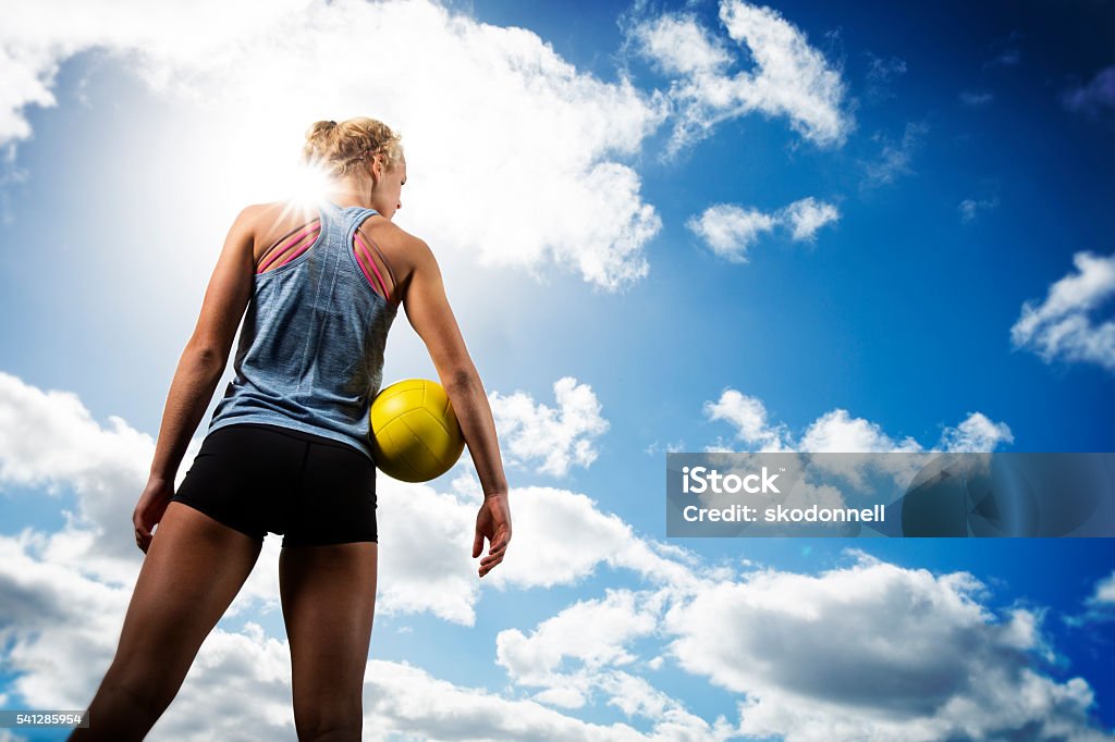 Beach Volleytball Girl Looking off This is a photo of the back of a teenage female athlete holding a ball on a beach volleyball court in a cloudscape setting. This photo is taken from a low angle capturing a great clouds in front of her and sun flare coming off her shoulder. She is looking out into the horizon. Volleyball - Sport Stock Photo