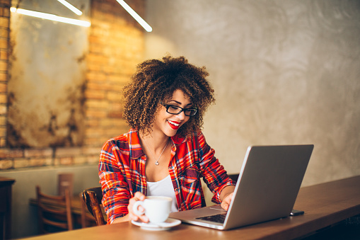 Young woman siting at cafe drinking coffee and working on laptop