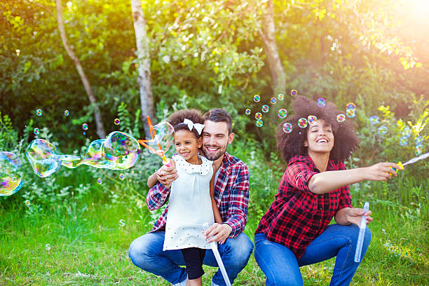 familia feliz jugando con burbujas de jabón en el parque. - bubble wand bubble child playful fotografías e imágenes de stock