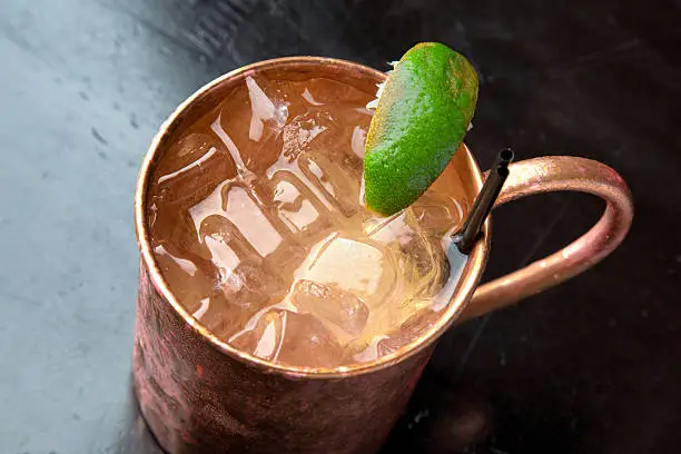 A cold icy Moscow Mule cocktail with vodka, ginger beer and lime in a traditional frosty copper mug