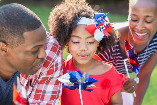 A mixed race African American family celebrating an American patriotic holiday, perhaps Memorial Day or July 4th. They are playing with red, white and blue pinwheels. The little girl in the middle, 7 years old, is part black, Asian and Hispanic.