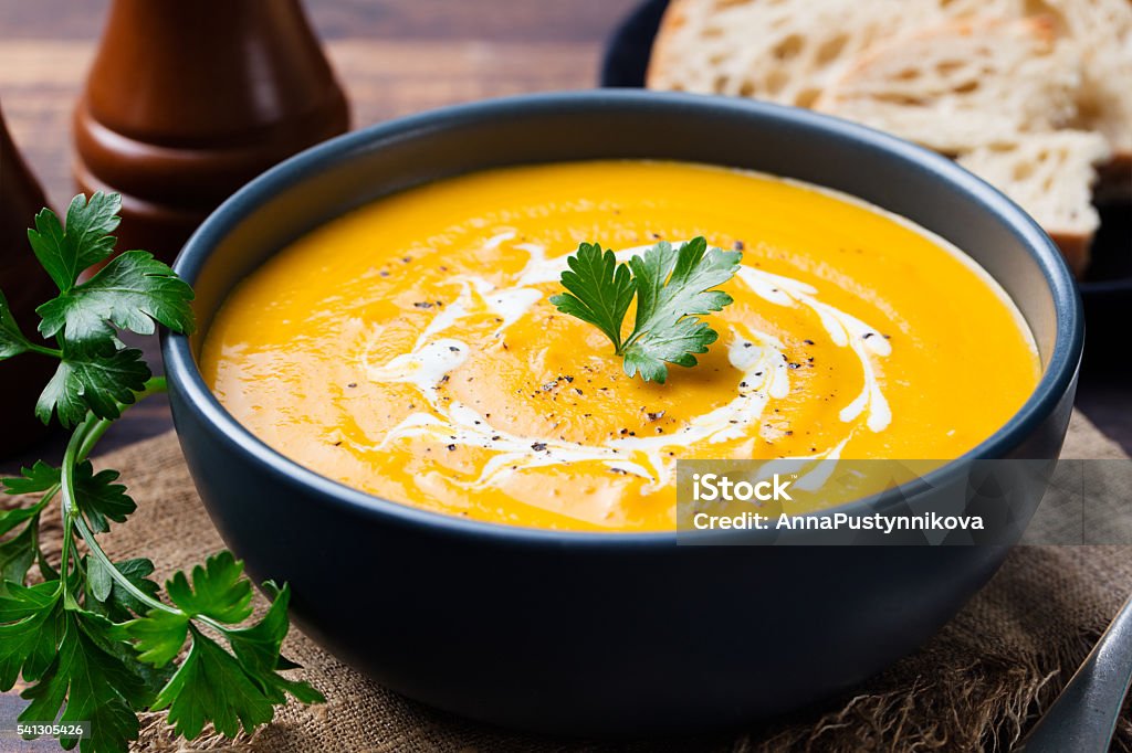 Pumpkin and carrot soup with cream and parsley Pumpkin and carrot soup with cream and parsley on dark wooden background. Soup Stock Photo