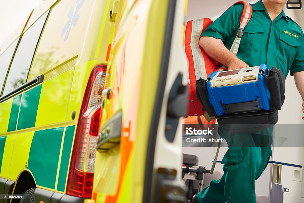 paramedic and ambulance a uk ambulance staff member emerges from the back of an ambulance with his emergency backpack , and vital signs monitor . Ambulance Stock Photo