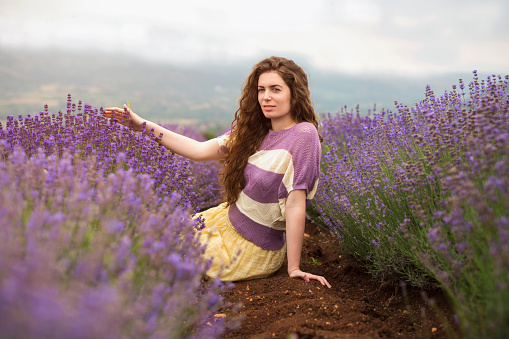 Beautiful young woman sitting in the middle of the lavender field, enjoying