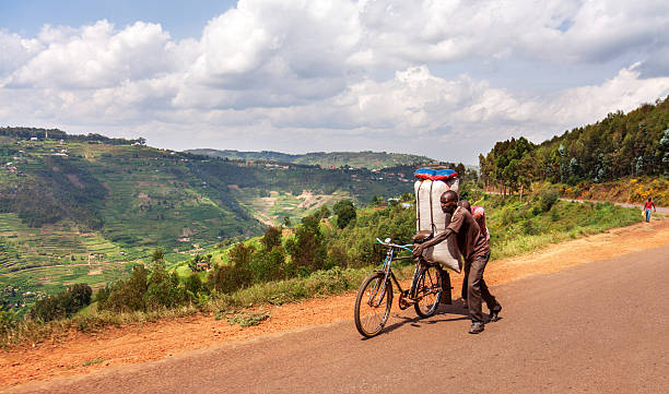 Along the road in Rwanda: cyclist on mountain road Gicumbi, Rwanda - June 3, 2016: a man walks his bicycle, loaded with a large bag uphill on the RN3 Byumba - Kigali road along the Muvumba river valley. In the background terraced fields against the hills. cycling rwanda stock pictures, royalty-free photos & images