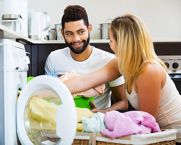 Mixed spouses doing regular laundry Positive young mixed spouses doing regular laundry and smiling at home laundry husband housework men stock pictures, royalty-free photos & images