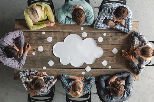 Hipster business teamwork brainstorming planning meeting concept, people sitting around the table with white paper shaped like dialog cloud