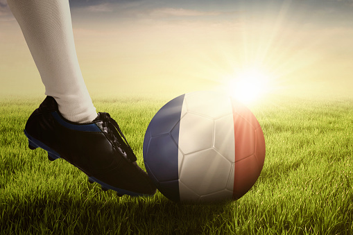 Soccer ball kicked by foot of football player at the field with sunlight background
