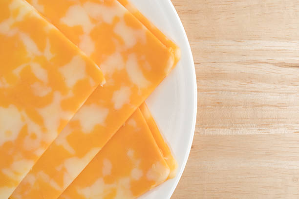 Colby-Jack cheese slices on a plate atop table Top close view of several slices of Colby-Jack cheese on a white plate atop a wood table illuminated with natural light. colby cheddar stock pictures, royalty-free photos & images