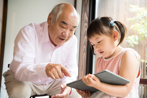 Young girl using digital tablet with grandfather pointing at screen