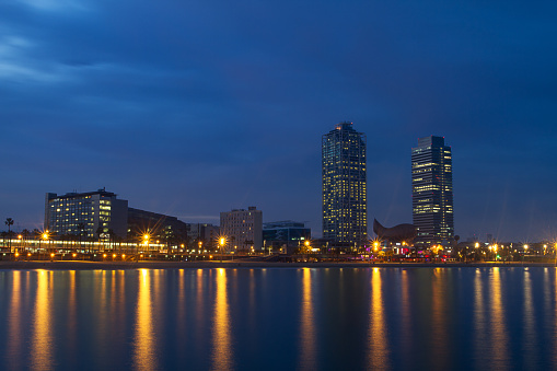 Barcelona night beach landscape with the city lights and skyscrapers . Water reflections of the citylights