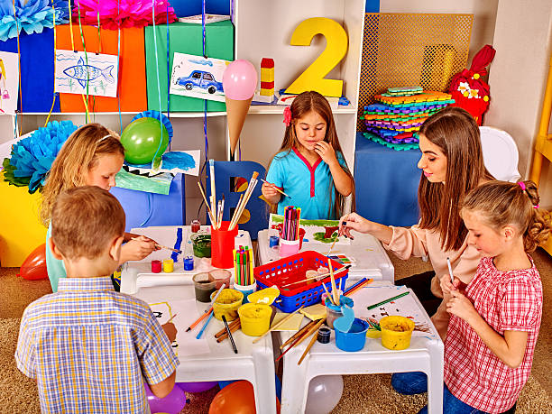 Children with teacher woman painting on paper in primary school . stock photo