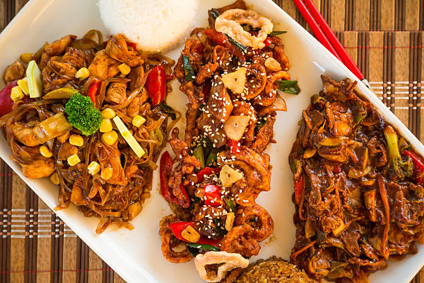 Three different Chinese meals served on white  plate: stir-fried chicken noodles with vegetables, , stir-fried squids and Asian beef with broccoli. Close-up, directly above image.