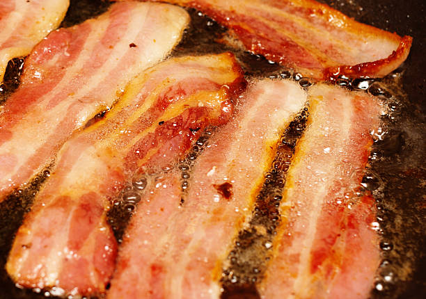 Bacon frying, delicious, paleo breakfast, high fat low carb, pork, Close up shot of appetizing sizzling rashers of bacon being fried. Banting or Paleo diet style breakfast coming up! saturated fat stock pictures, royalty-free photos & images