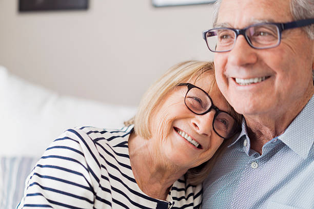 Senior woman leaning head on senior man's shoulder unreimbursed medical expenses Happy loving couple are looking away. They are wearing eyeglasses at home. age 60 stock pictures, royalty-free photos & images
