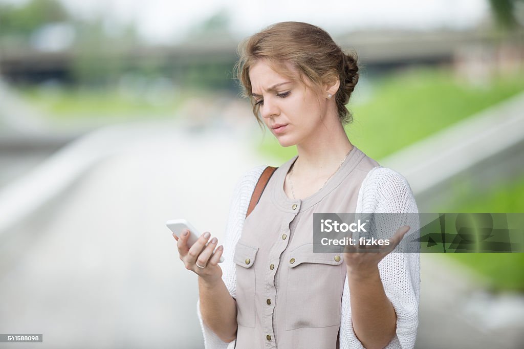 Portrait of stressed woman looking at smartphone screen outdoors Portrait of stressed beautiful caucasian woman walking on the street and looking at smartphone screen with irritated face expression. Attractive model using mobile phone outdoors in summer Telephone Stock Photo