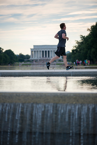 Washington DC, USA - June 20, 2016: A man listening to an iPod or similar audio device jogs on the Mall in Washington DC between the National World War Two Memorial and the Lincoln Memorial.