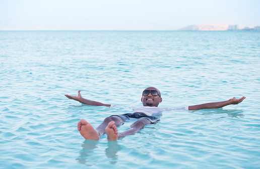 Tourist enjoying his vacation in Dead Sea. Man floating on salty lake, looking at camera with a friendly smile.
