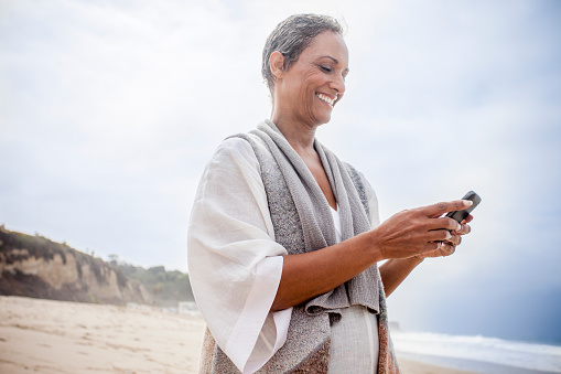 A senior African American woman checks her phone on the beach.