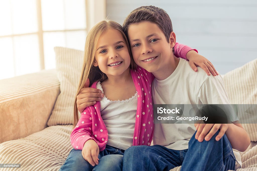 Sister and brother Cute little girl and her brother are hugging, looking at camera and smiling, sitting on sofa at home Brother Stock Photo