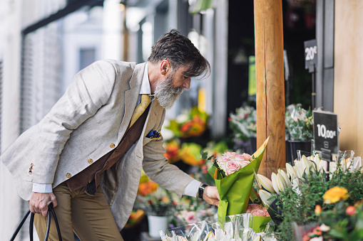 French mature man buying flowers in flower shop at Paris.