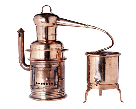 Old vintage copper alembic used for the distillation of liquids with two vessels, one with a burner, connected by a tube isolated over white