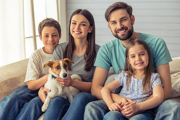 Family at home Beautiful young parents, their cute little daughter and son are looking at camera and smiling, sitting with their cute dog on sofa at home young family photos stock pictures, royalty-free photos & images