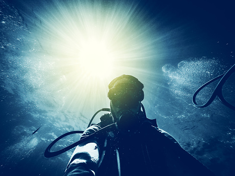 Man doing scuba diving in the ocean with sunbeam in the background entering into the water.