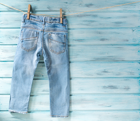 Baby boy blue jeans hanging on a clothesline on blue wooden background